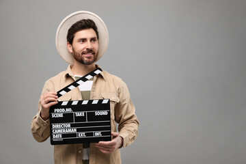Smiling actor holding clapperboard on grey background, space for text