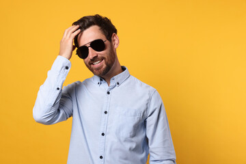 Portrait of smiling bearded man with stylish sunglasses on orange background. Space for text