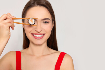 Funny young woman holding sushi roll with chopsticks on light background. Space for text