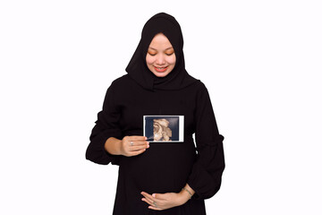 Happy Pregnant Young Hijab Woman holding showing ultrasound scan photo. Pregnant woman hands holding belly on white background.