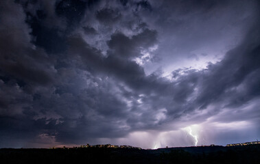 Beautiful thunderstorm with clouds and lightning over the night city - 566552715
