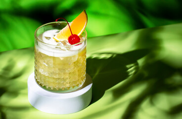 Whiskey sour alcoholic cocktail with bourbon, lemon juice, egg white and ice, rocks glass on bright green background with hard light and shadows