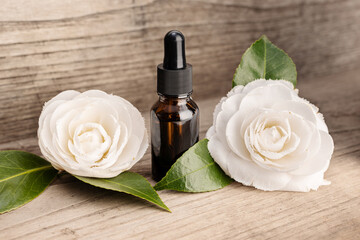 Camellia essential oil still life. Amber bottle and camellia flowers on rustic wooden table