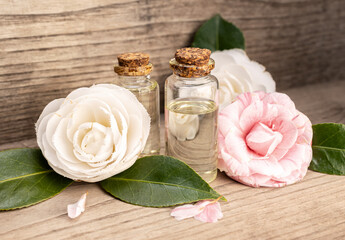 Obraz na płótnie Canvas Camellia oil bottles and camellia flowers on rustic wooden table