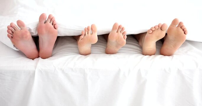 Legs of woman with two men in bed in bedroom