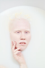 Young serene albino woman with no makeup on her face relaxing in bathtub filled with warm water and milk and taking pleasure - obrazy, fototapety, plakaty