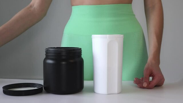 Close up of women with measuring scoop of whey protein and shaker bottle, preparing protein shake. A girl pours BCAA into a sports cup. The concept of sport, relaxation and muscle growth.