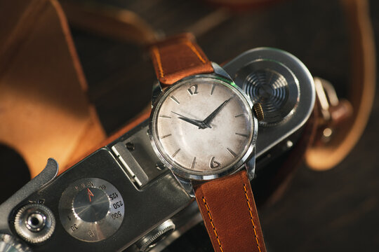 Vintage men's Omega dress watch with white rustic dial and brown leather strap laying on the vintage photocamera.