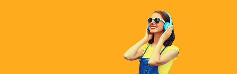 Portrait of happy smiling young woman with headphones listening to music on yellow background