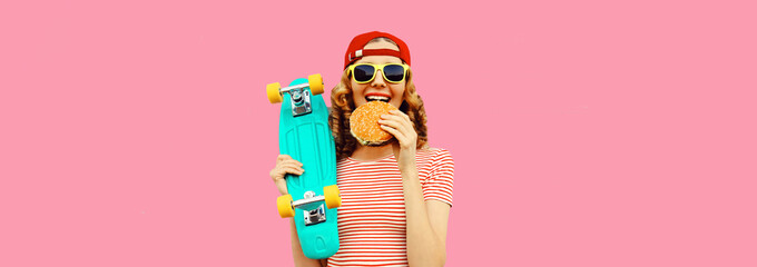 Portrait of stylish young woman with burger fast food and skateboard wearing baseball cap, sunglasses on pink background