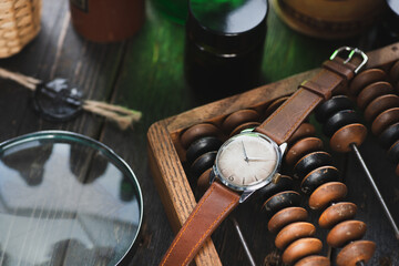 Vintage men's Omega dress watch with white dial and brown leather strap laying on the wooden abacus near to the magnifying glass and black wax stamp on the brown wooden rustic surface in a daylight.