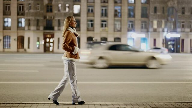 slender single woman walks along a busy highway in the city at night