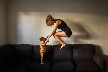Playful mom jumping on large couch holding hands with her child