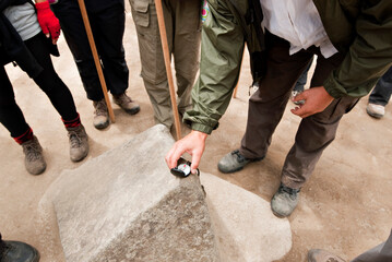 A young man places a compass on a rock that the Incan's perfectly carved in the four cardinal directions to use for navigation.