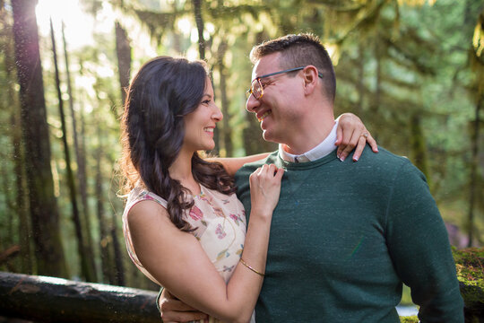 Smiling couple embracing in forest on hiking trail that parallels McKenzie River at Sahalie Falls, Oregon, USA