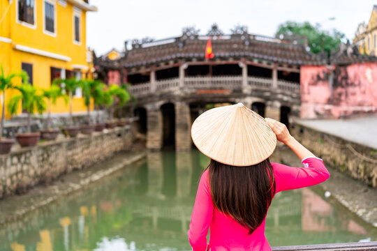 Young female tourist in Vietnamese traditional dress walking at Hoi An Ancient town in Vietnam