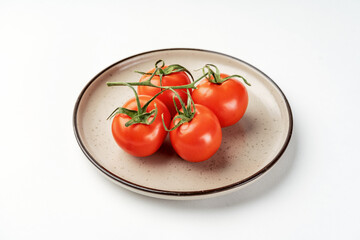 Red tomatoes on a branch in a ceramic plate on a light background closeup