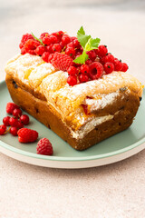 Rich sweet pie with fresh fruits, decorated with red currants and raspberries, in a plate on a pink background