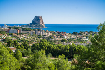Obraz premium view from Olta mountain on small houses, trees and apartment buildings and Ifach rock and Mediterranean sea