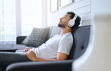 Music, relax and man with headphones on sofa in home living room streaming radio or podcast. Meditation, technology and male on couch in lounge listening to peaceful song, audio or album in house.