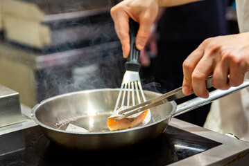 man chef cooking fried salmon fish in frying pan on kitchen