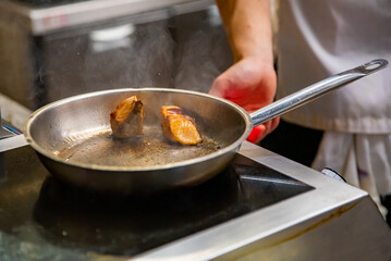 man chef cooking fried salmon fish in frying pan on kitchen