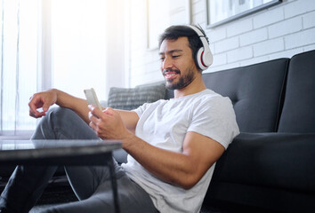 Phone, music and man with headphones in home living room streaming radio or podcast. Cellphone, technology and male in lounge sitting on floor listening to song, audio or album on mobile smartphone.