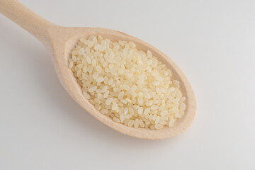 Round grain rice in wooden spoon on a white background