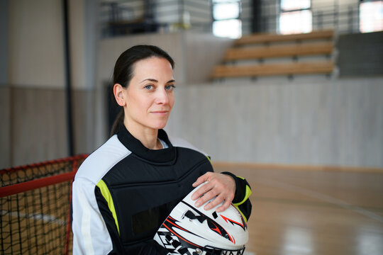 Close-up of woman floorball goalkeeper in helmet concetrating on game in gym.