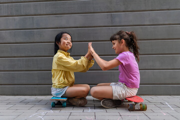 Obraz na płótnie Canvas Asian girl with her friend sitting in skateboards in city street, talking and playing, active lifestyle kids concept.