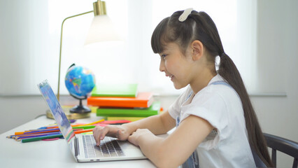 Portrait of happy young smiling child kid girl, Asian Thai woman studying at home with computer laptop notebook device online, people lifestyle.