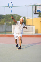 Senior man playing badminton outdoor at badminton court. Concept of active lifestyle being on pension