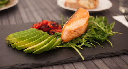 dish of cooked salmon fillet with fresh vegetables and herbs on a black stone plate