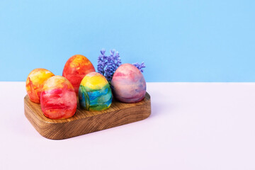 Colorful Easter eggs in a wooden egg stand on a blue and pink background with a place for text. Happy Easter concept. Greeting card.