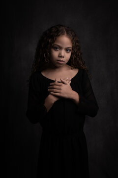 classic dark painterly fine art studio portrait of young girl in black dress with curly hair