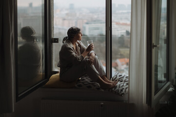 Young unhappy woman with cancer sitting in a window and looking at view.