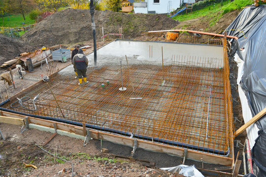 Bauarbeiter gießen die Bodenplatte eines Einfamilienhaus-Neubaus über der Baustahlmatte mit der Betonpumpe