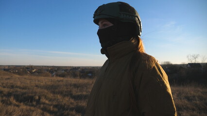 Female ukrainian army soldier walking at the field. Woman in military uniform and helmet going on...