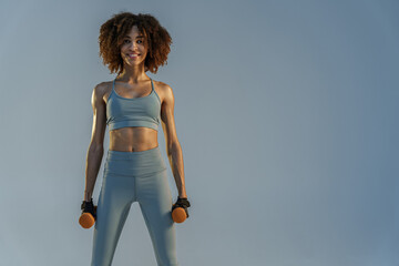 Athletic woman doing exercise with weight dumbbells on studio background. Strength and motivation