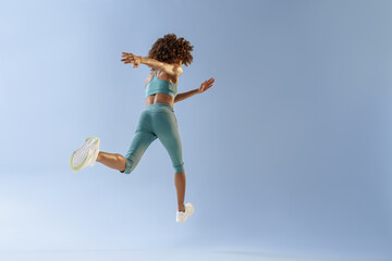 Back view of sporty woman running in Mid-Air exercising during cardio workout over studio background
