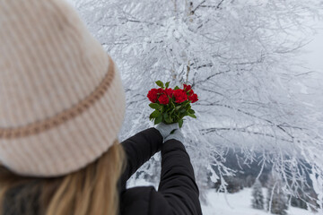 Fototapeta na wymiar Woman holding a bouquet of red roses in the winter forest