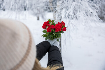 Red roses in the hands of a girl on a background of winter forest. Valentine's day concept. 