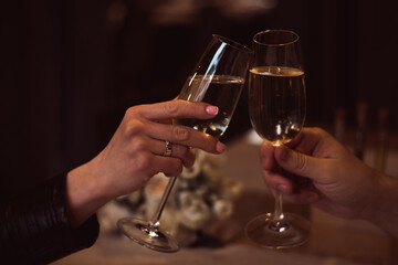 Two glasses with sparkling champagne wine in hands, concept for holiday, bokeh, in a restaurant. Romantic dinner. Man and woman are holding glasses of champagne. Concept for Valentine's day or date.