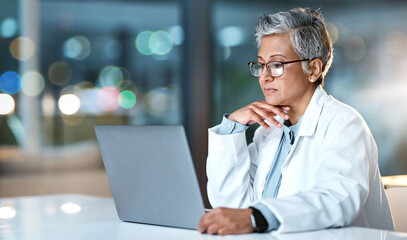 Laptop, doctor and senior woman in hospital working late or overtime on email, telehealth or research. Bokeh, thinking and female medical physician reading healthcare information at night on computer - Powered by Adobe