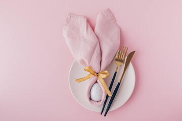 Happy Easter table setting with egg in napkin Easter Bunny and golden cutlery.