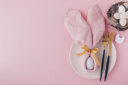 Happy Easter table setting with egg in napkin Easter Bunny and golden cutlery.