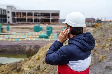 Man a civil engineer, in a hard hat, speaks on the phone. Construction of a large industrial building