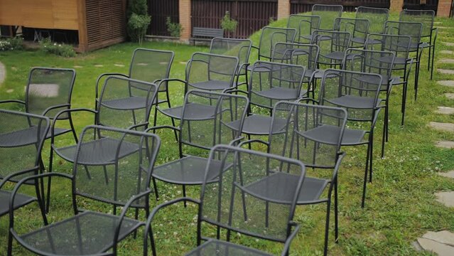 Close-up of black empty chairs at the wedding ceremony in a park, green lawn on the background, slow motion.