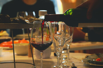 Pouring red wine from bottle into  glasses on table with food background