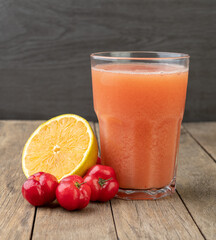 Acerolas or Barbados Cherries and orange juice with fruits over wooden table